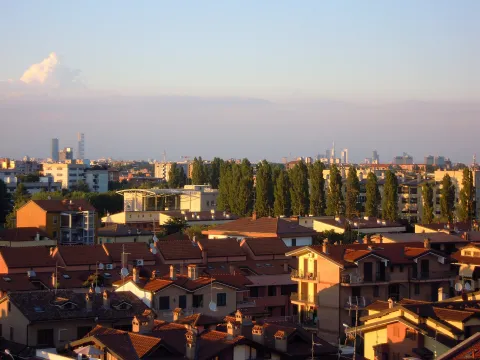 View of Buccinasco rooftops with the distant skyline of Milan at sunset