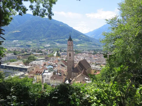 Panoramic view of Merano featuring St. Nicholas Church tower and surrounding mountains