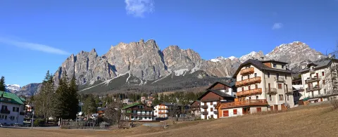Traditional alpine buildings in Cortina d'Ampezzo with dramatic Dolomite mountain peaks behind.