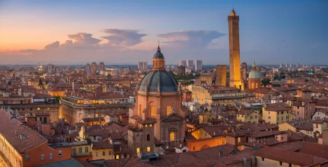 Panoramic skyline of Bologna at sunset featuring the Two Towers and Santa Maria della Vita dome
