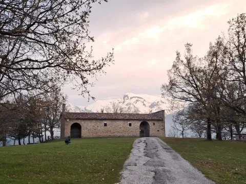 Rustic stone building in a grassy field with snow-capped mountains behind