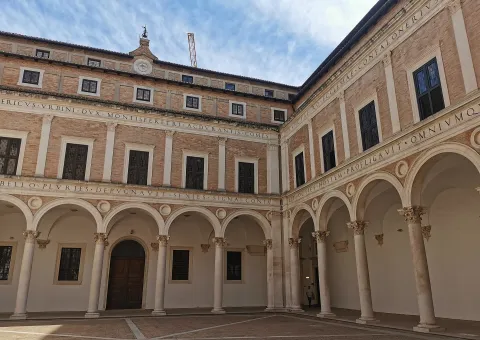 Cortile d'Onore del Palazzo Ducale di Urbino con porticato rinascimentale ed iscrizioni in latino.