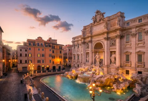 La Fontana di Trevi illuminata all'alba a Roma, vista sulla piazza e l'edificio barocco.