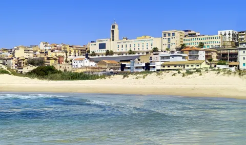 Golden sand beach with a view of the skyline of the coastal town of Gela, Sicily.