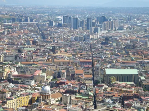 High-angle view of Spaccanapoli cutting through the historic center of Naples toward modern skyscrapers.