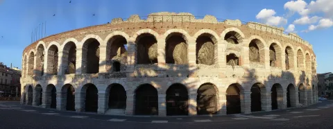 The Verona Arena displaying its iconic Roman stone arches under a clear blue sky.