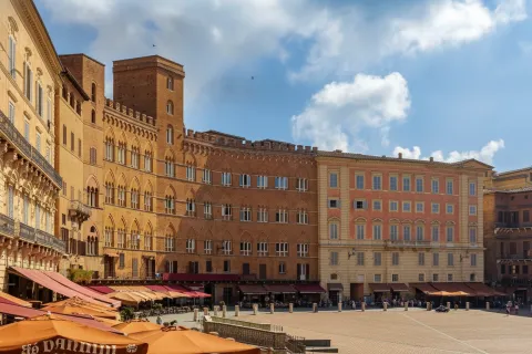 Historic brick buildings and outdoor cafes surrounding Piazza del Campo in Siena, Italy.