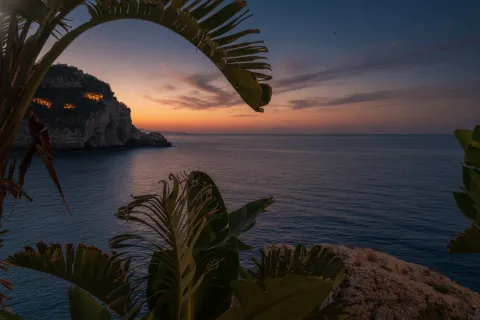 View of the sea and coast near Isola Bella in Taormina framed by tropical foliage.