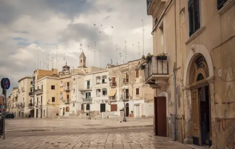Sunlit square in Bari Vecchia with historic stone buildings and a parked scooter