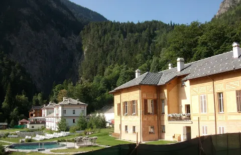 Historic thermal spa building and outdoor pool at Terme di Pré-Saint-Didier surrounded by mountains.