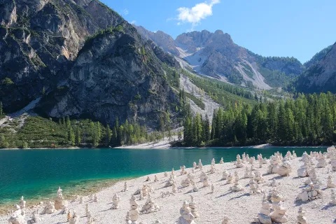 Stone cairns on the pebble beach of Lago di Braies with turquoise water and majestic peaks.