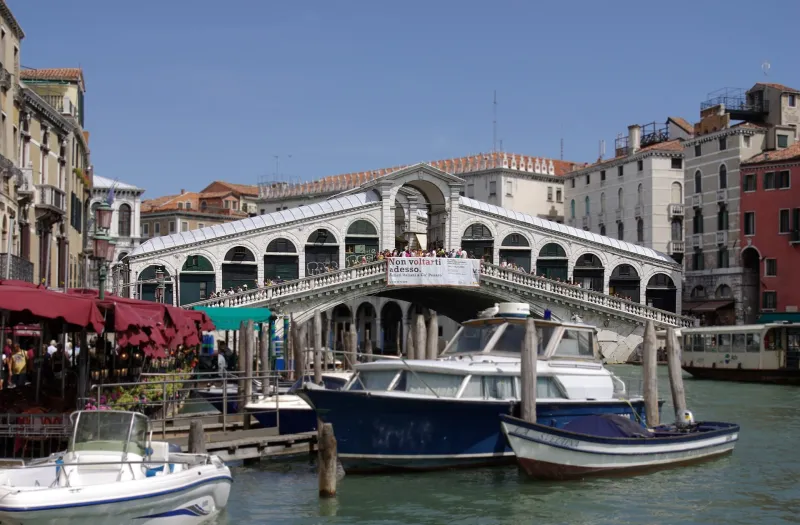 Rialto Bridge over the Grand Canal in Venice with boats moored in the foreground.