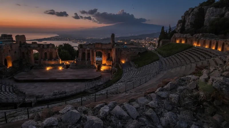 Vista del Teatro Antico di Taormina al tramonto con la costa e il mare sullo sfondo.